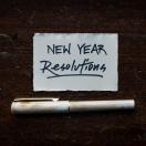 a piece of paper that reads "new year resolutions" with a pen placed below it on a black background