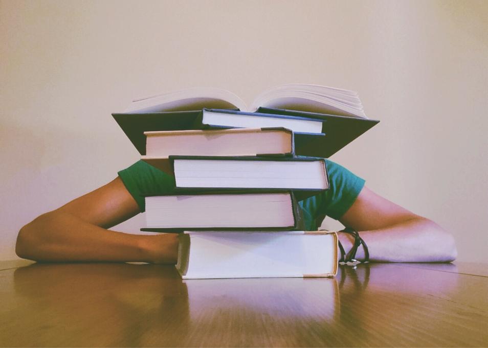 person sitting behind a stack of books at a desk