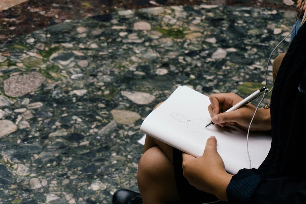 person sitting and sketching in a notebook