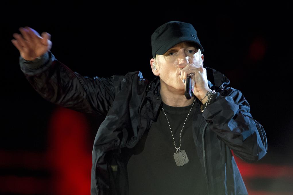 Eminem performing while wearing a black shirt, jacket and hat
