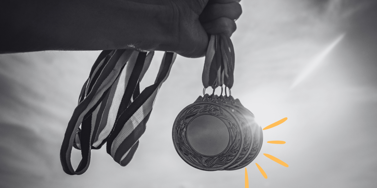 black and white image of a hand holding 3 medals with orange line doodles