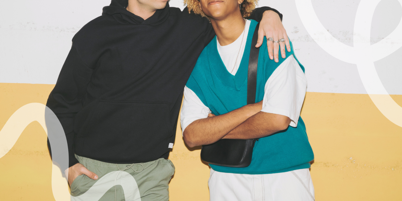 two guys one with his arm around the other leaning up against the wall