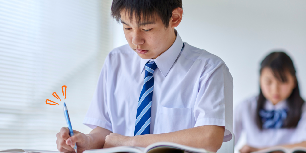 a teen male student wearing a uniform writing with a pen in a workbook