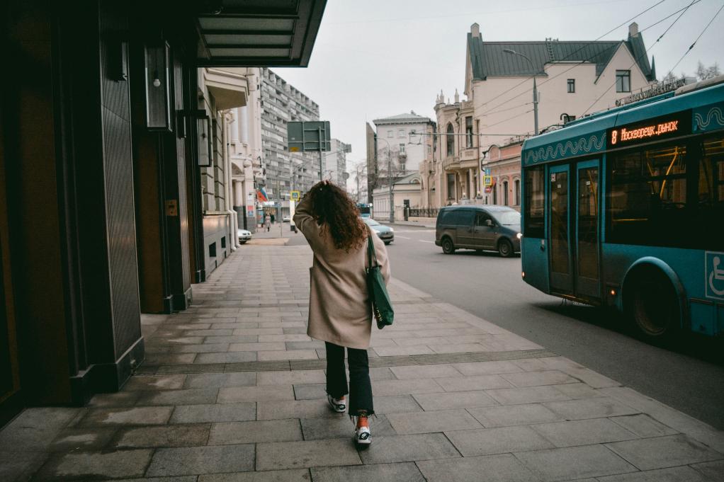 woman walking down a city street faced away from the camera with a bus passing by