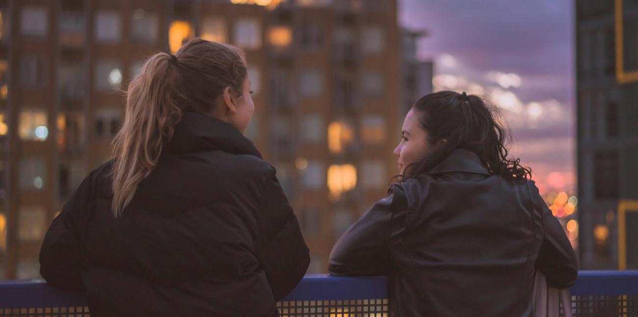 two young women on a roof overlooking the city one of them looking at the other