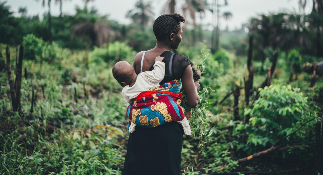 a mother walking with a child strapped to her back