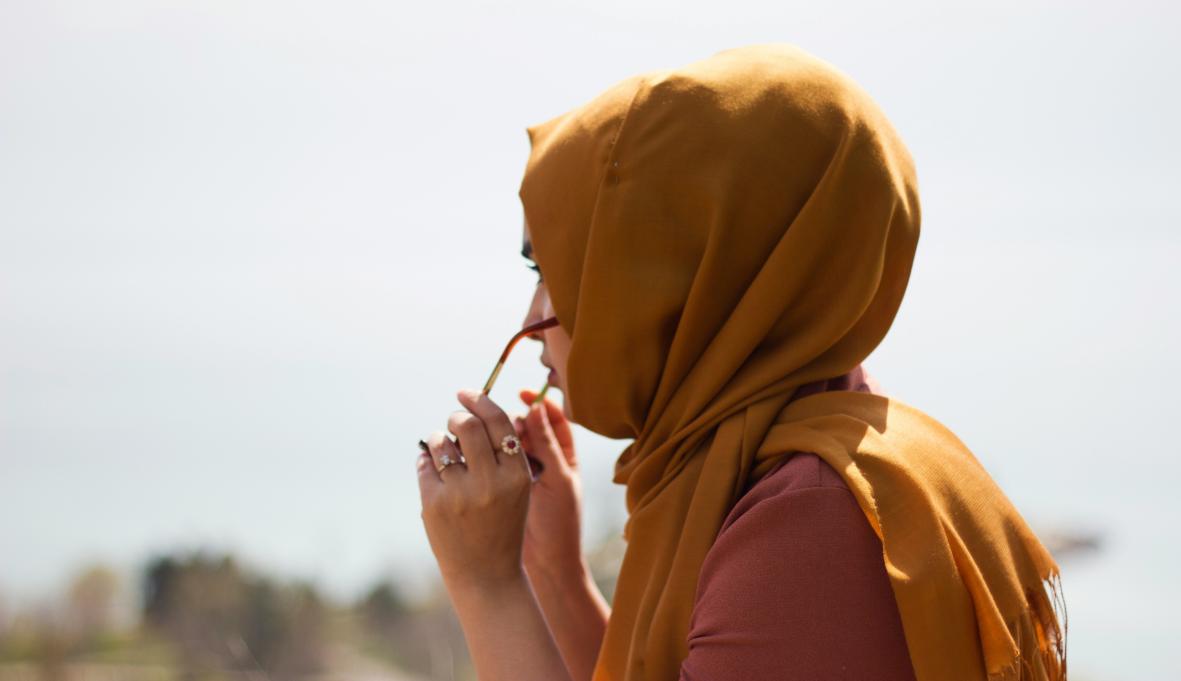 a young woman wearing an orange hijab, putting on sunglasses
