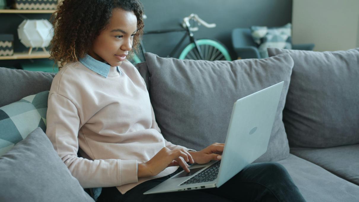 a young woman sitting on a couch typing on a laptop