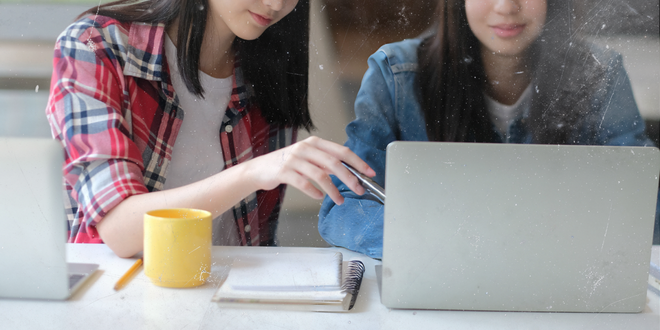 two young women sitting at a desk looking at a laptop