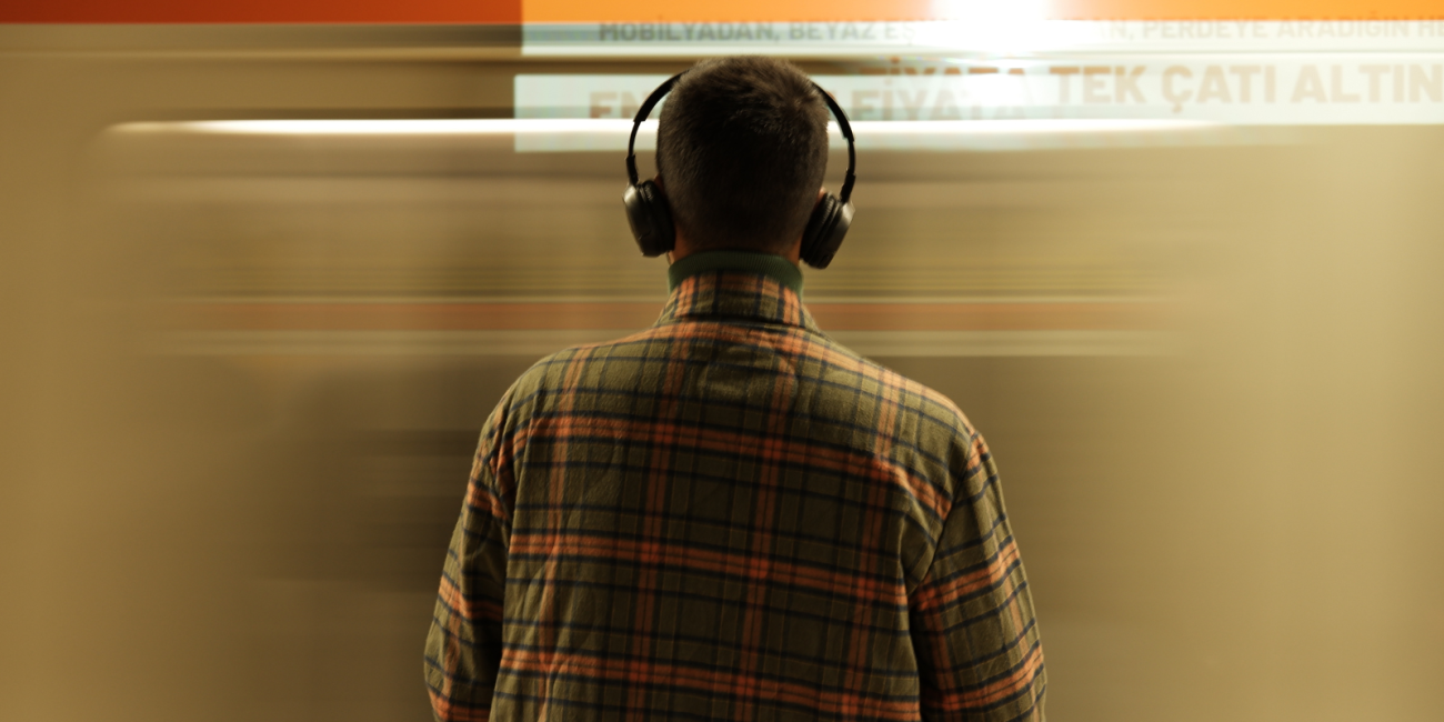 young man standing in front of moving train wearing headphones