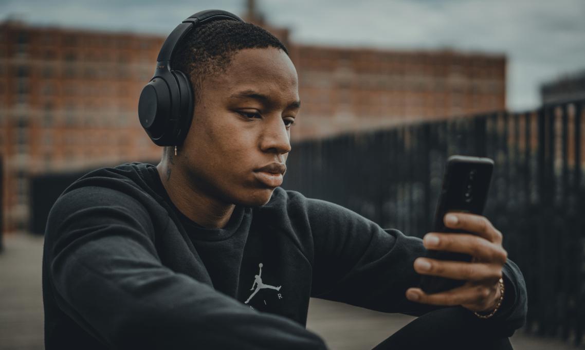 A young man wearing headphones looking at his phone