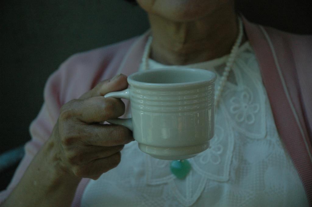 an elderly woman holding a white teacup
