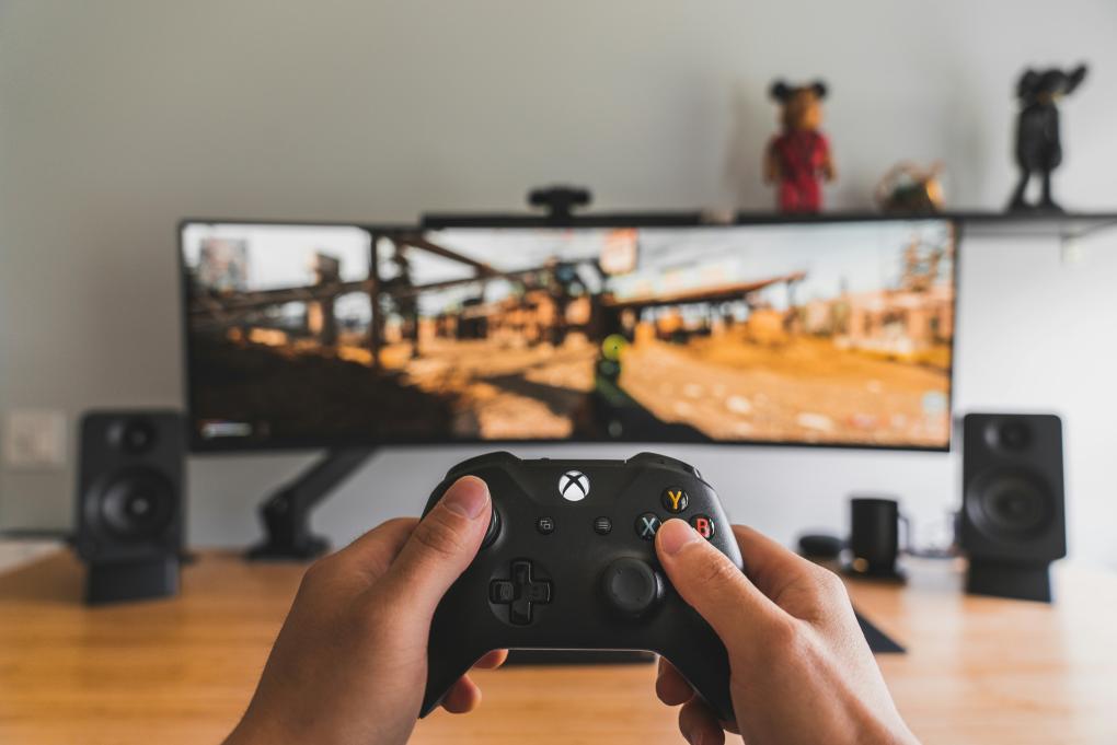 hands holding up xbox controller in front of a monitor displaying a video game