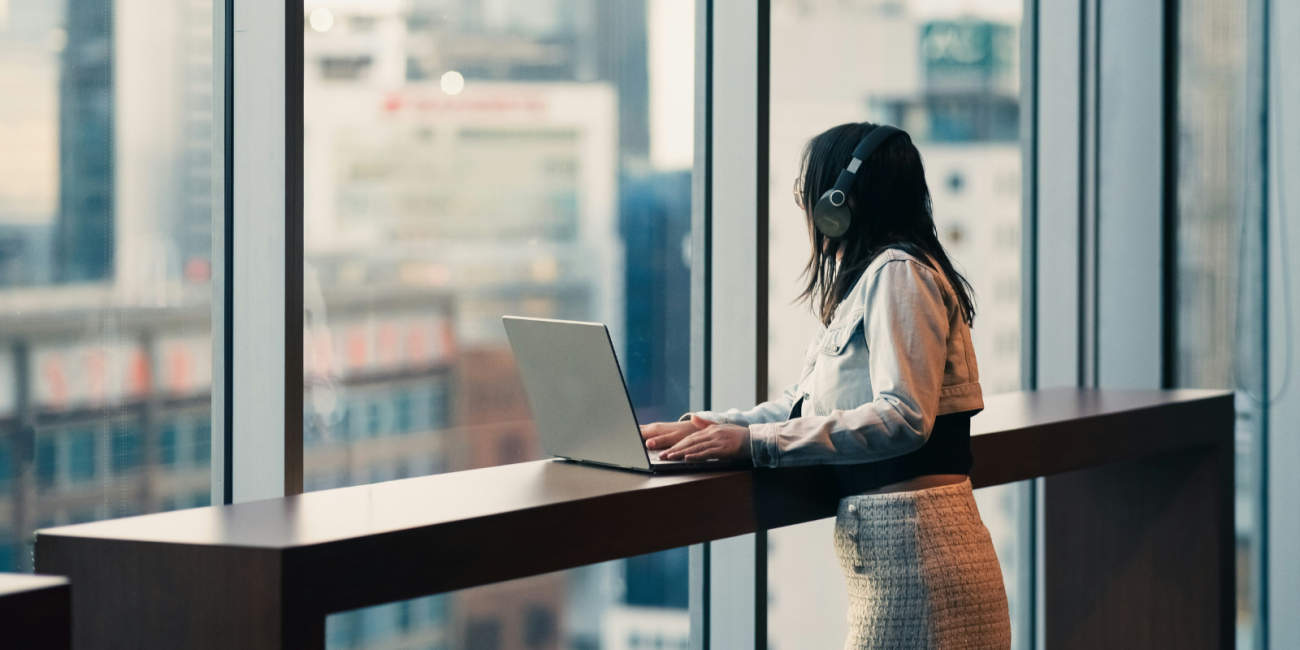 young woman looking out the window in a high rise office as she works on her laptop