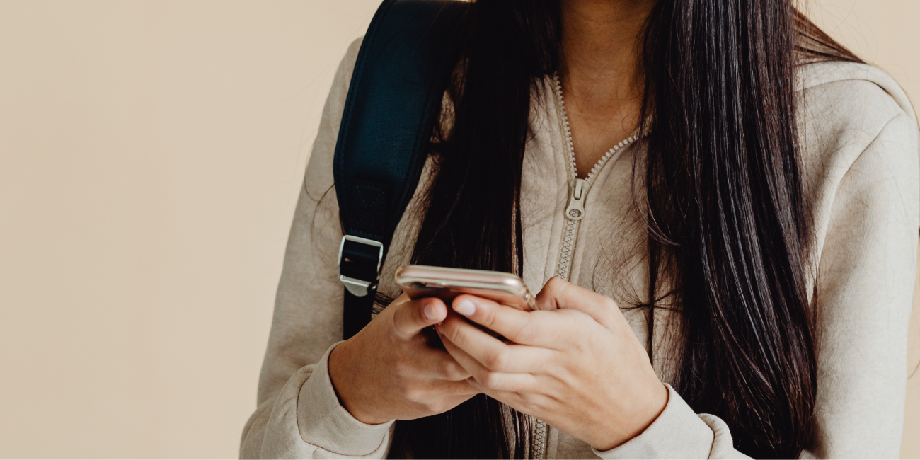a young woman wearing a beige jacket holding her phone