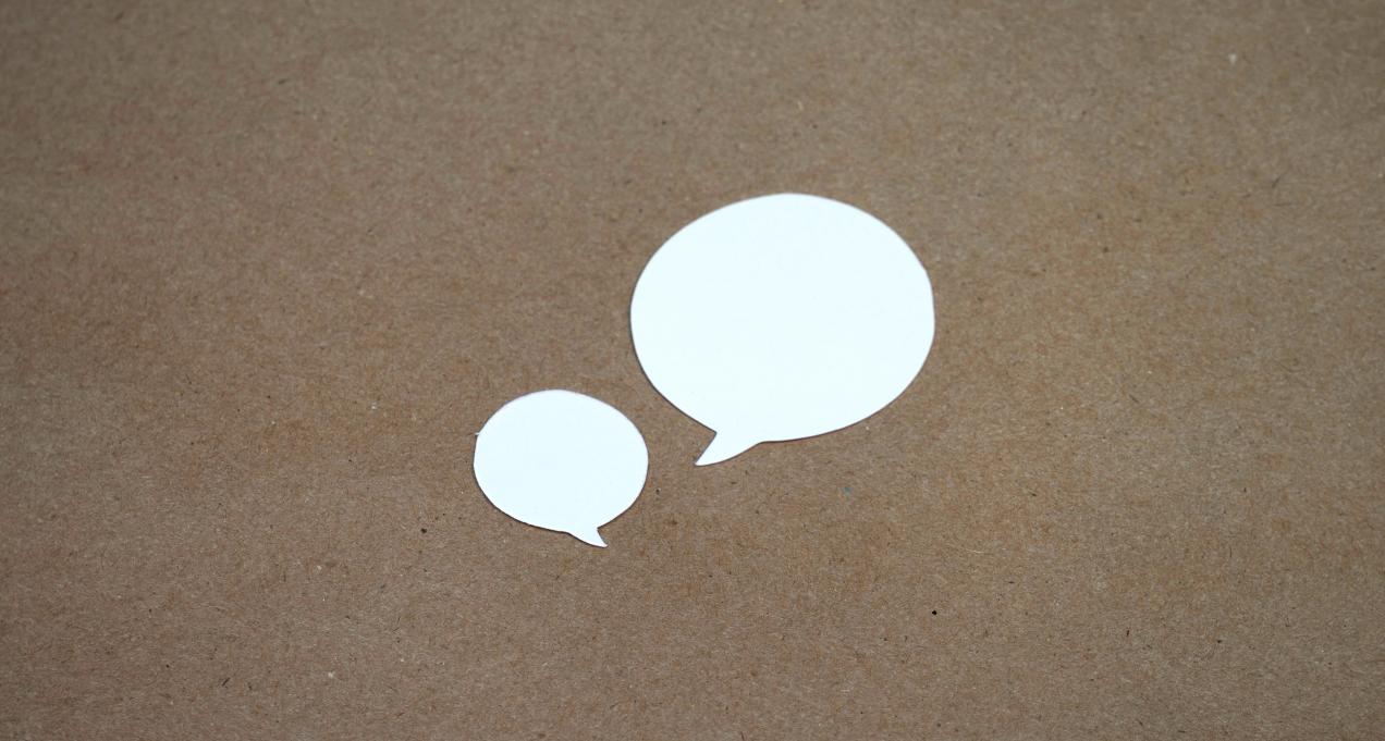 two paper speech bubbles on a plain bulletin board
