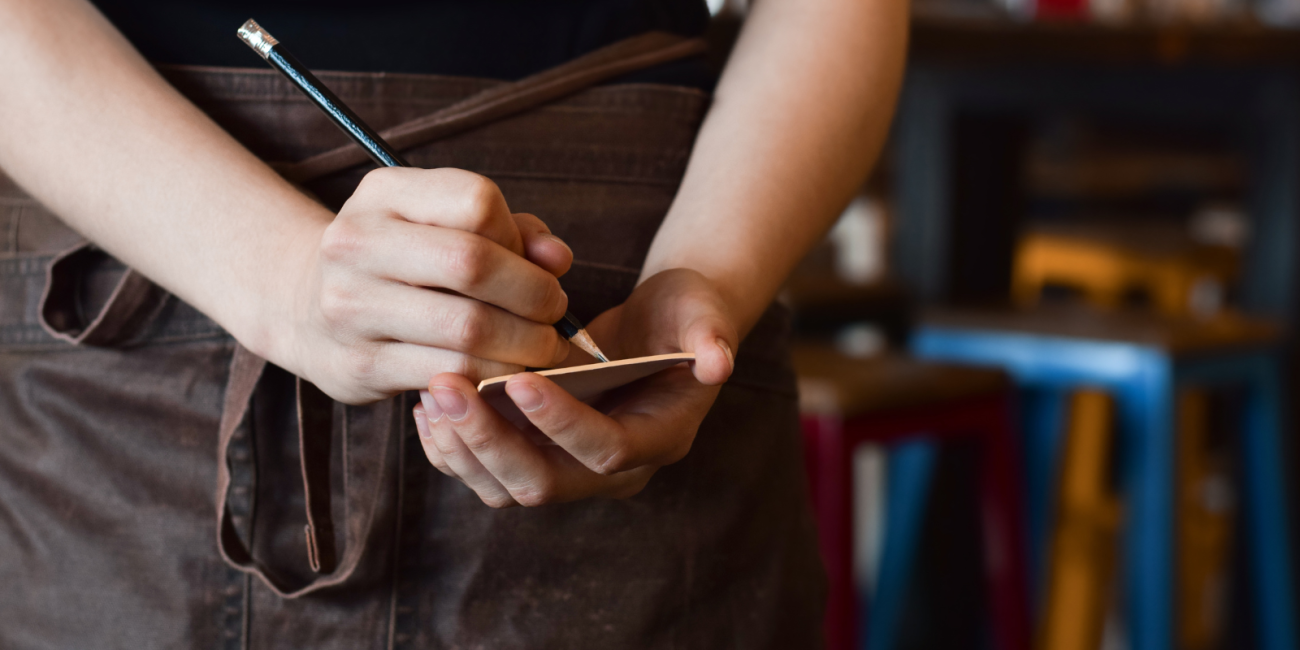 a young person writing down an order on a notepad while wearing an apron