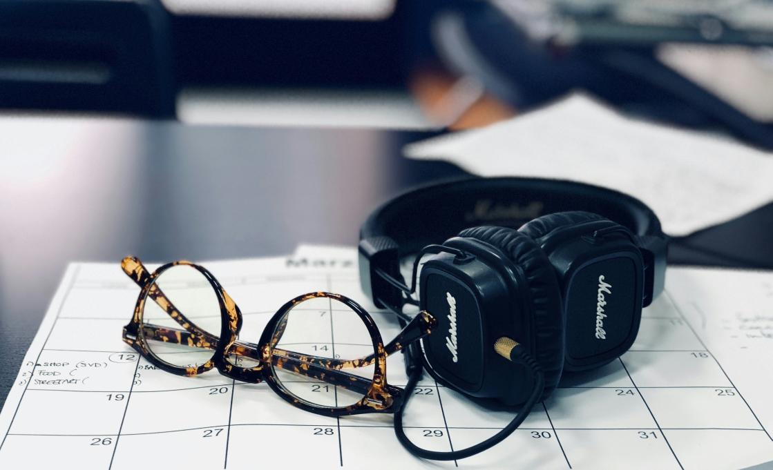 headphones, glasses and a calendar sitting on a desk