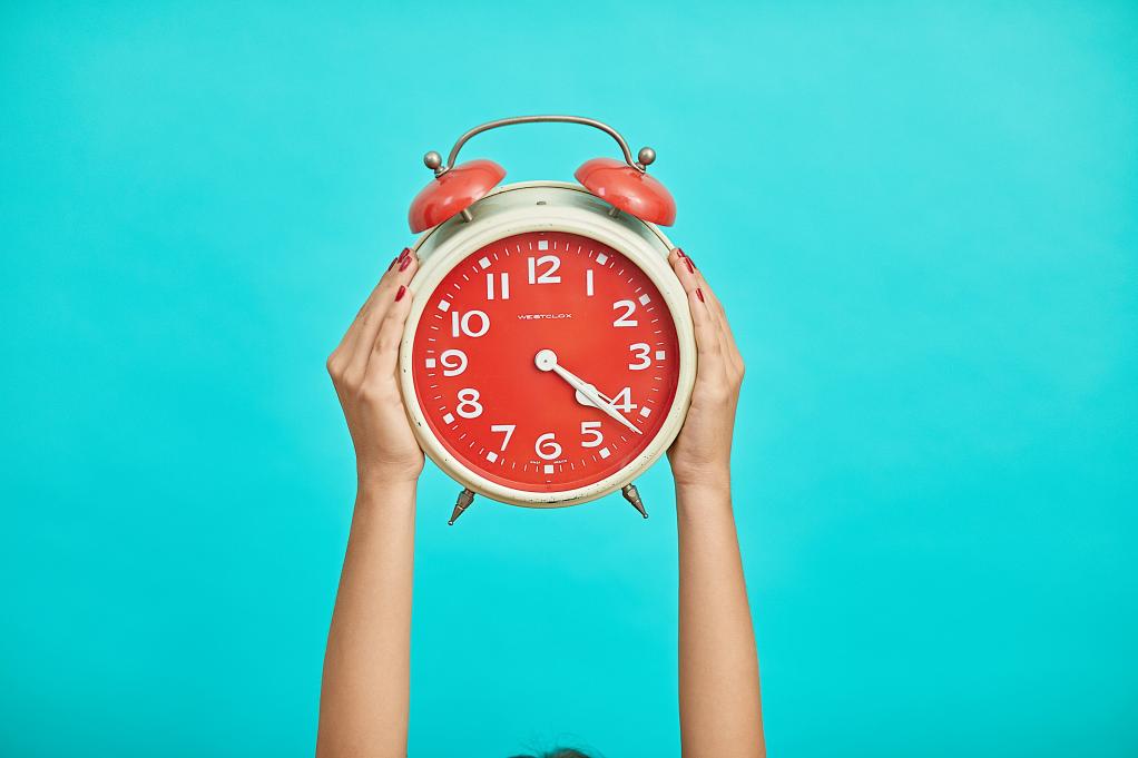 Hands holding up an alarm clock on a blue background