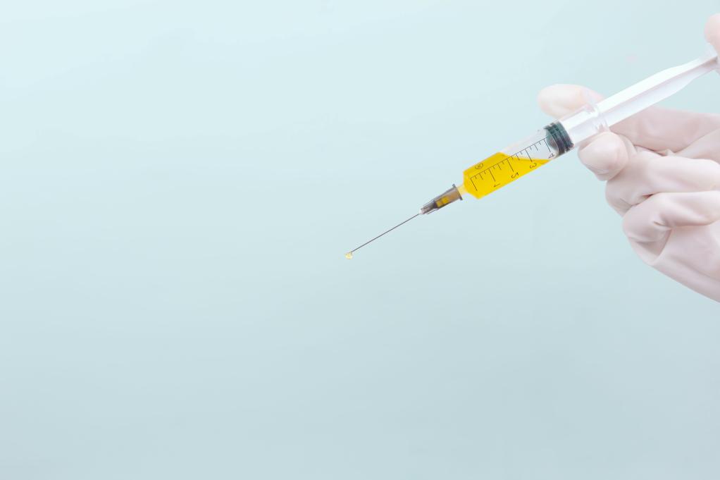 an image of a hand holding a syringe filled with a yellow liquid