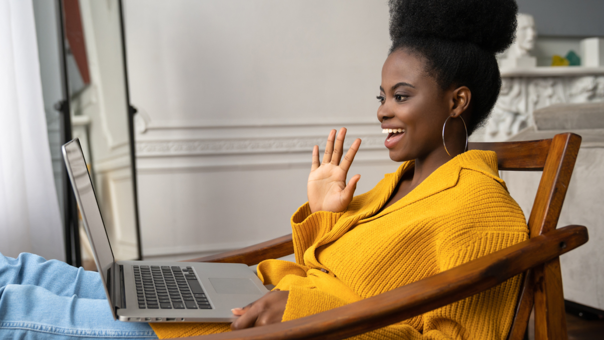 black woman on a video call waving at a laptop