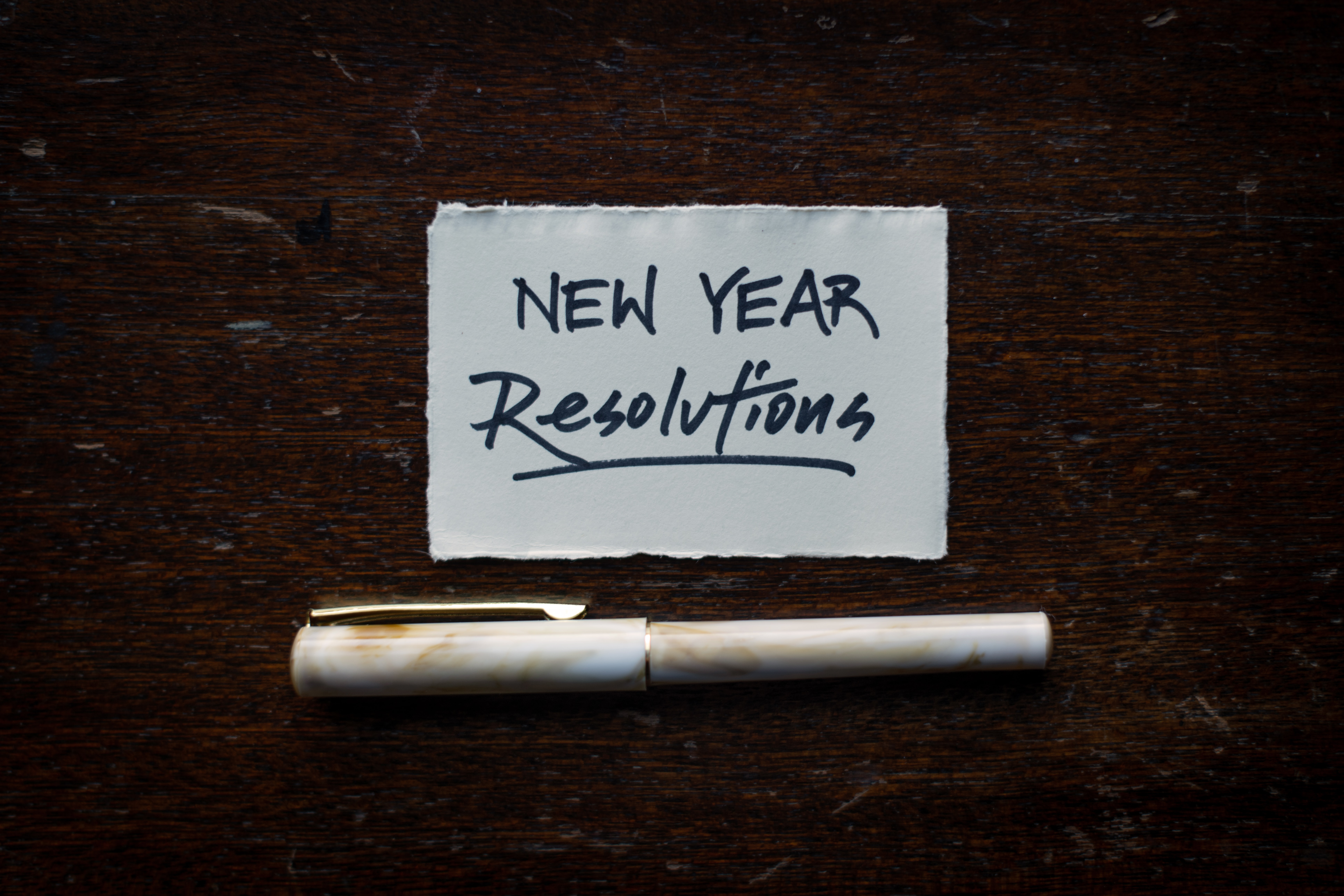 a piece of paper that reads "new year resolutions" with a pen placed below it on a black background